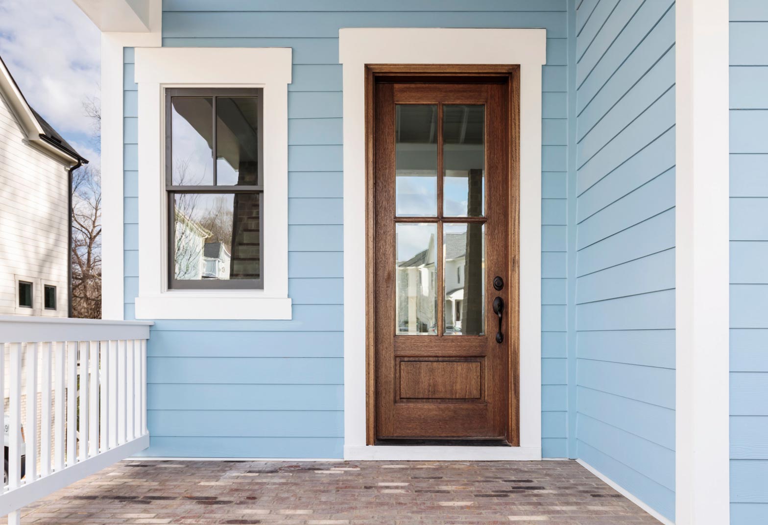 door-1 A wooden front door with glass panels graces the blue house, crafted by skilled home builders beside a white-trimmed window and an inviting porch.