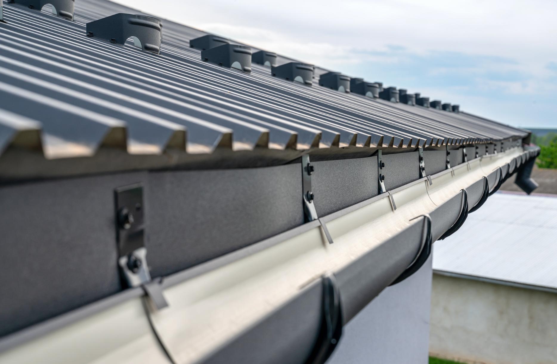 gutter-2 Metal roof with rain gutters attached, viewed from an angle by skilled home builders in Rockville. Sky and distant buildings in the background add to this MD home's charm.