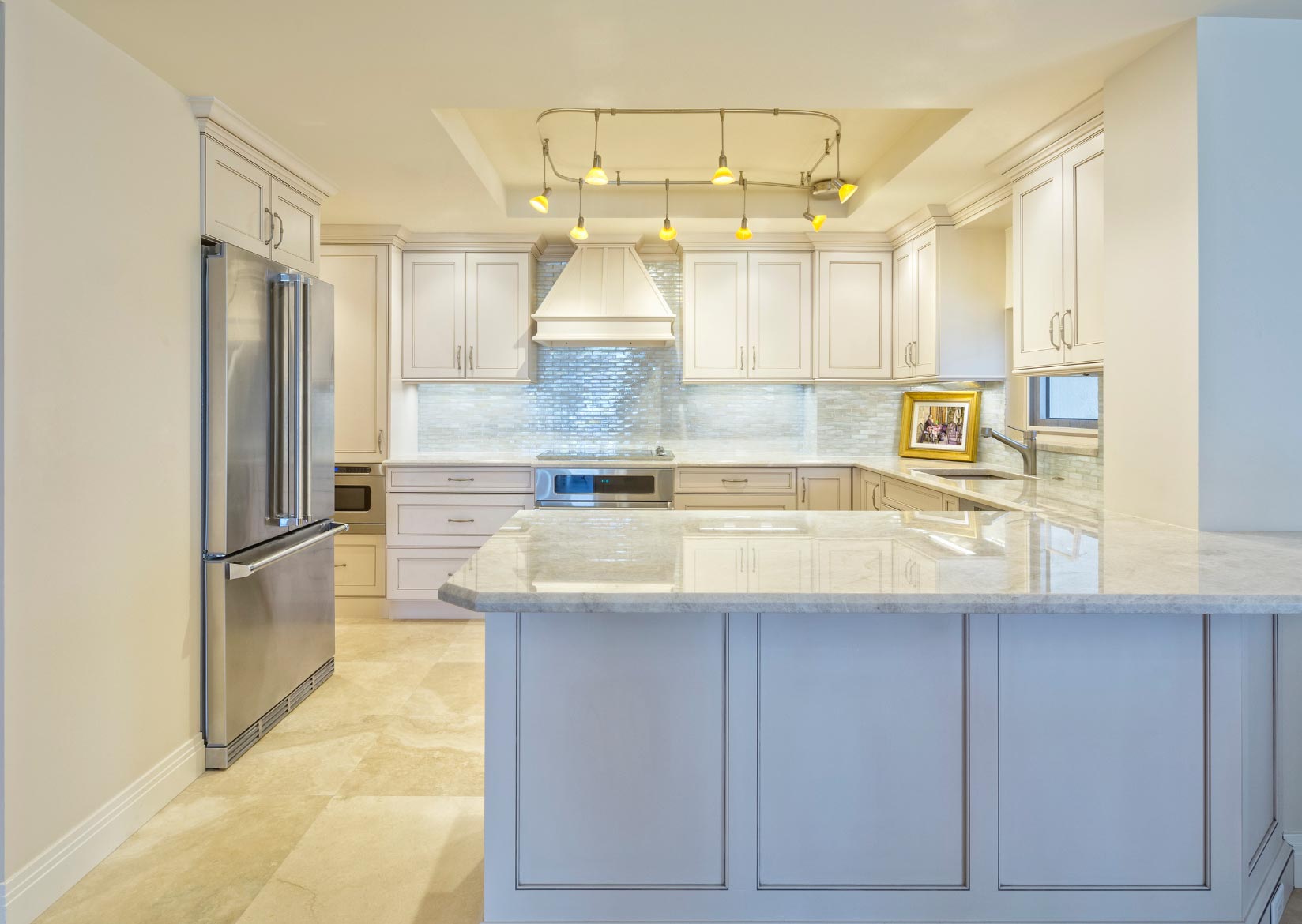 Modern kitchen with white cabinets, stainless steel appliances, marble countertops, and overhead track lighting.
